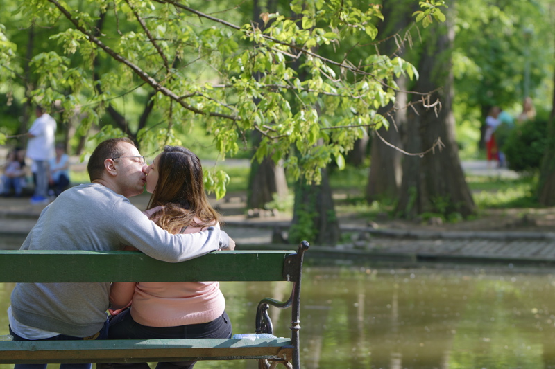 1 - A couple kissing while sitting on a park bench by a lake